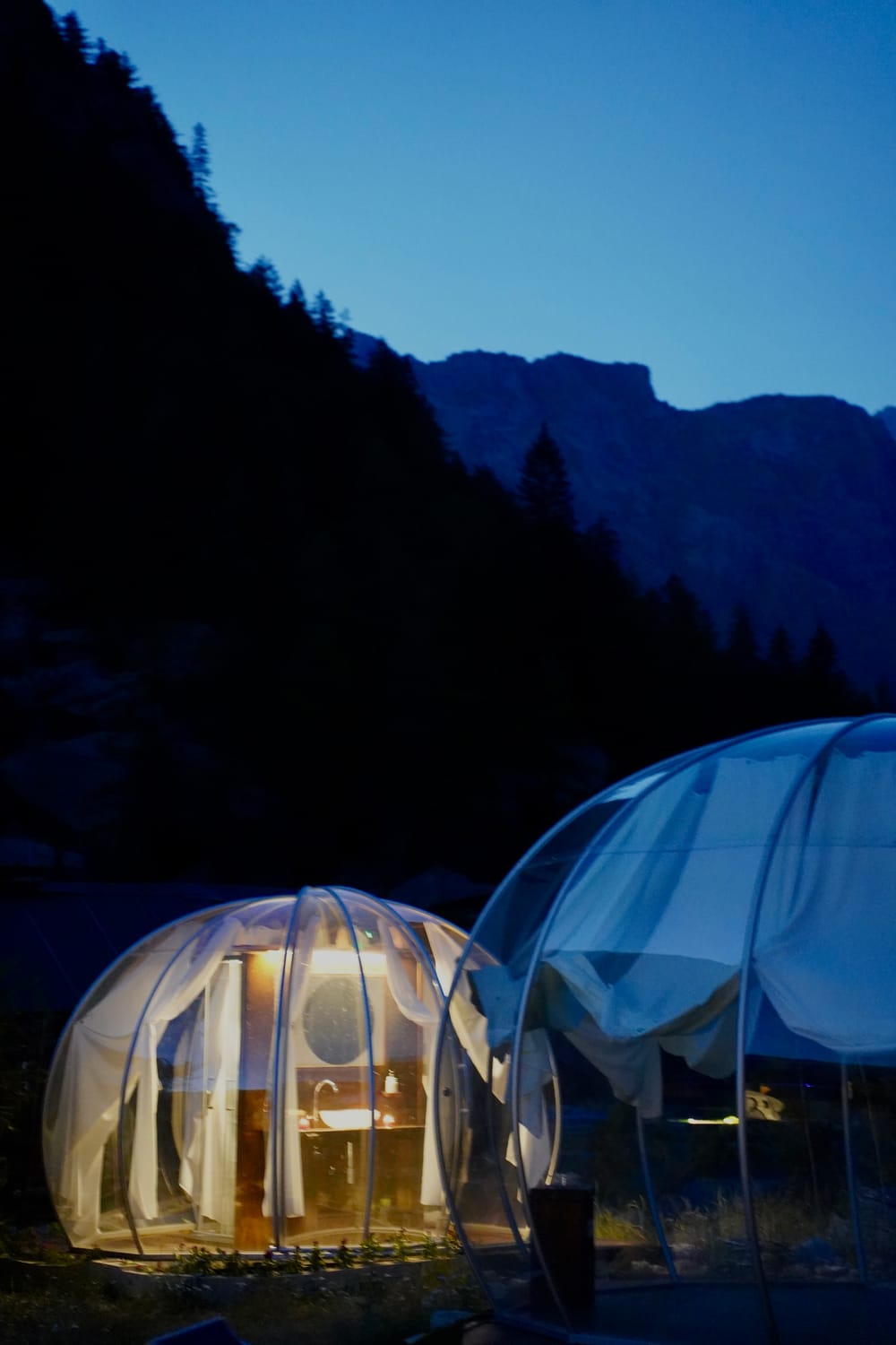 Bolla glamping trasparente al crepuscolo tra le montagne